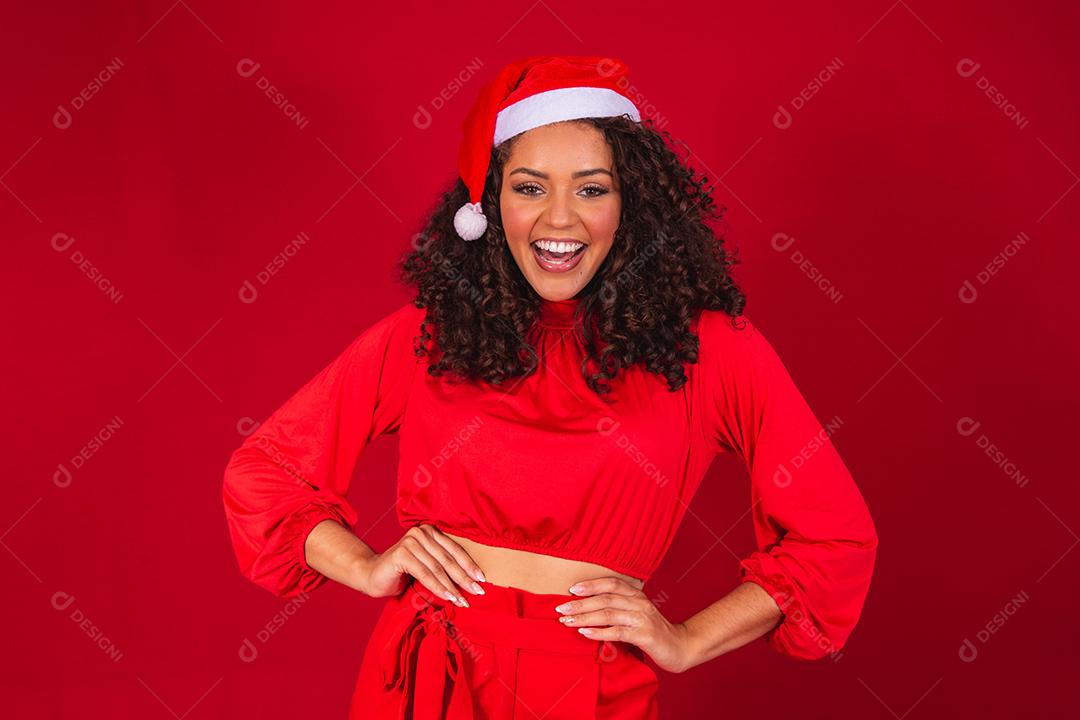 Feche a foto de uma jovem afro usando chapéu de Papai Noel isolado sobre fundo vermelho.