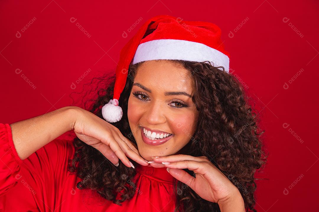 Feche a foto de uma jovem afro usando chapéu de Papai Noel isolado sobre fundo vermelho.