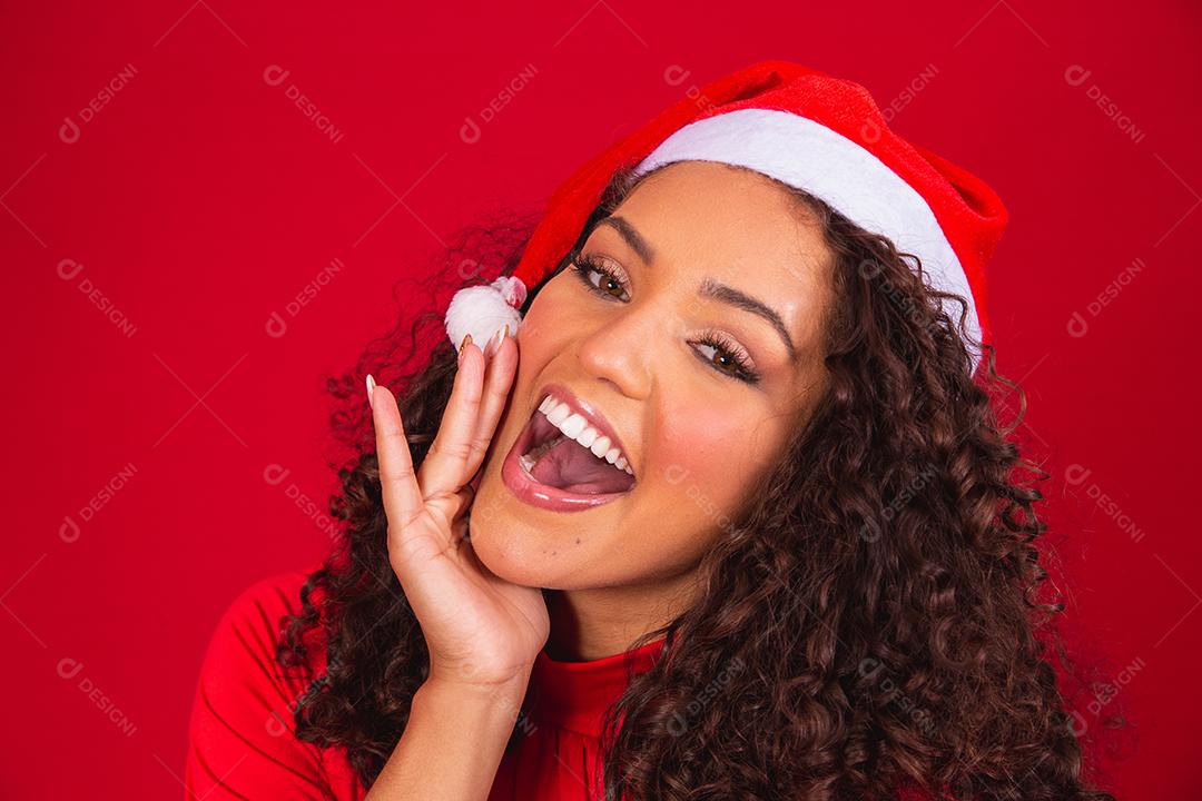 Feche a foto de uma jovem afro usando chapéu de Papai Noel isolado sobre fundo vermelho.