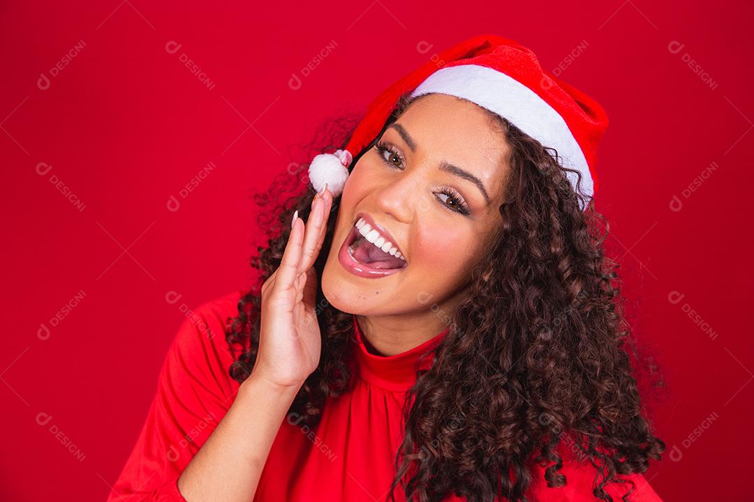 Feche a foto de uma jovem afro usando chapéu de Papai Noel isolado sobre fundo vermelho.