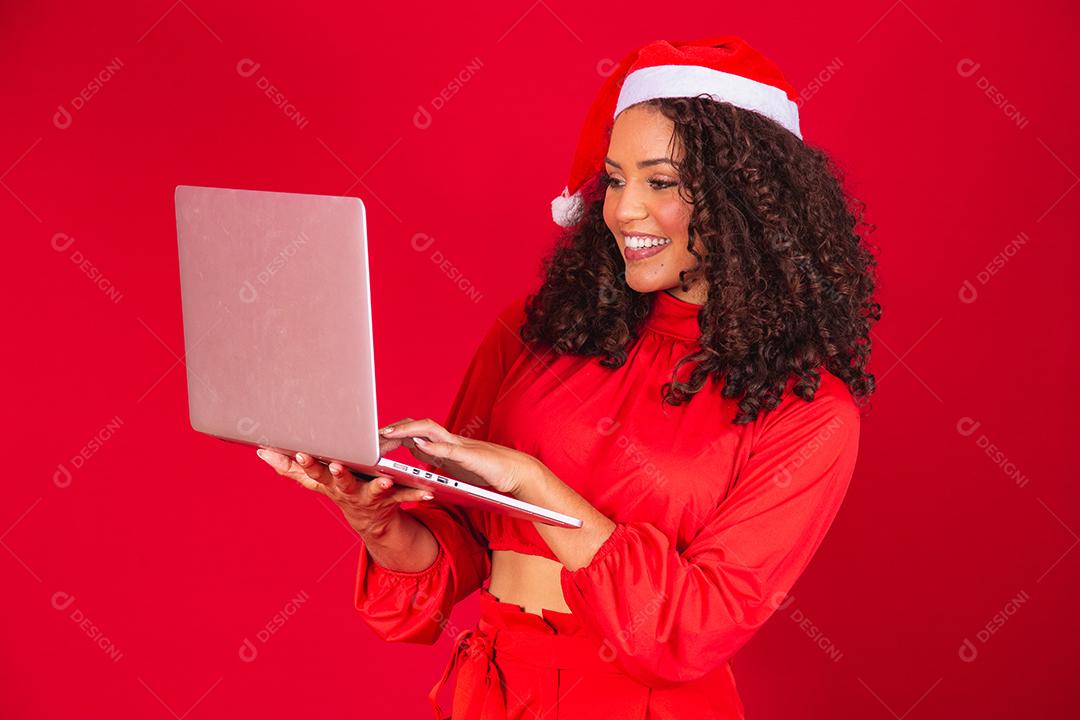 Mulher comemorando o natal em fundo vermelho e fazendo uma chamada de vídeo no laptop