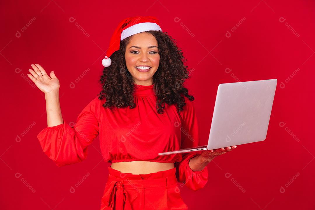Mulher comemorando o natal em fundo vermelho e fazendo uma chamada de vídeo no laptop