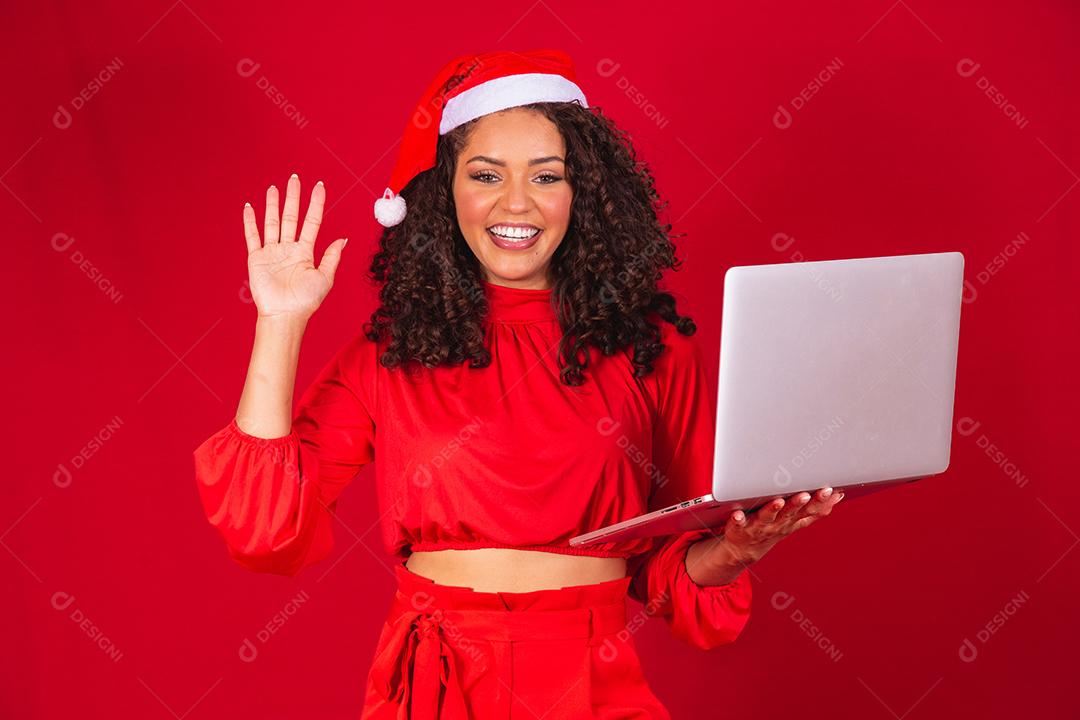 Mulher comemorando o natal em fundo vermelho e fazendo uma chamada de vídeo no laptop