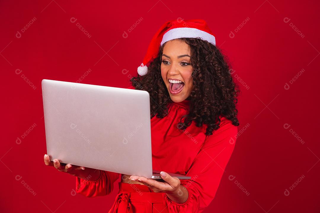 Mulher comemorando o natal em fundo vermelho e fazendo uma chamada de vídeo no laptop