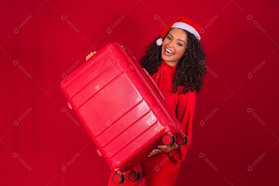 Mulher com chapéu de natal sorrindo e segurando mala vermelha