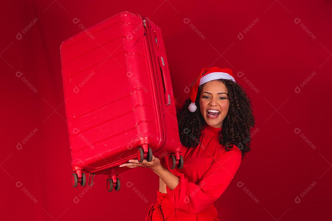 Mulher com chapéu de natal sorrindo e segurando mala vermelha
