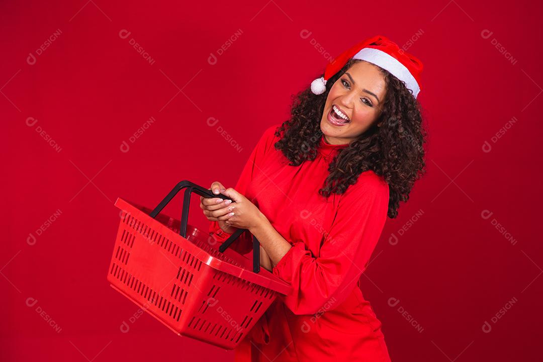 Mulher com chapéu de natal sorrindo e segurando cesta de compras vazia