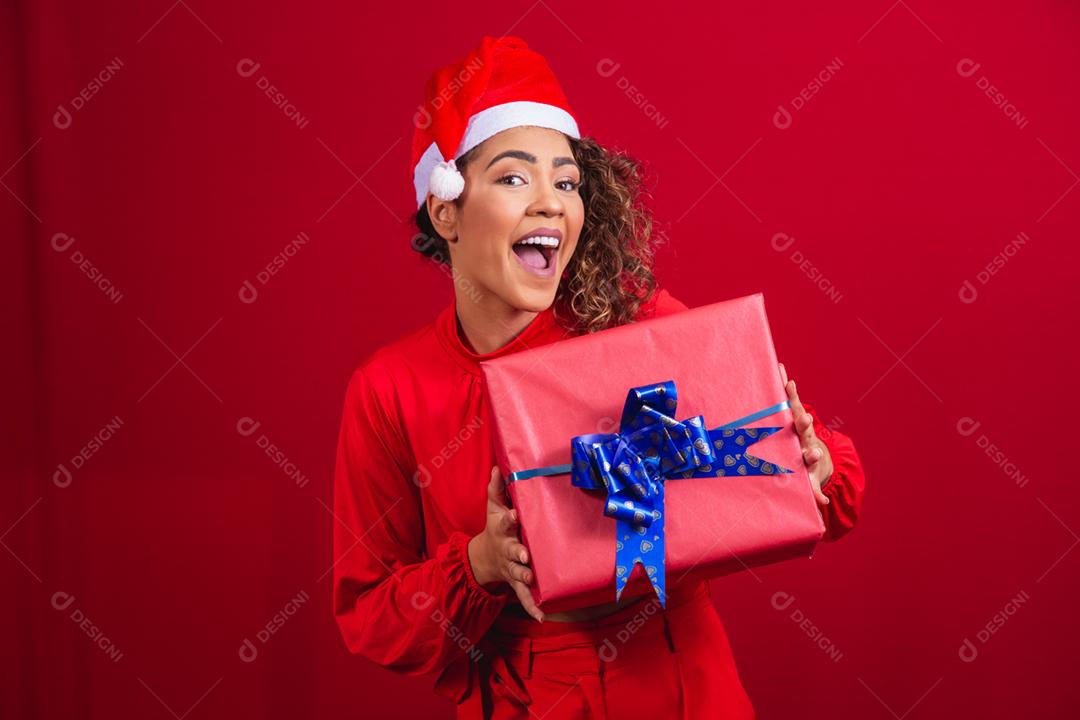 Retrato de jovem afro com chapéu de papai noel segurando um presente