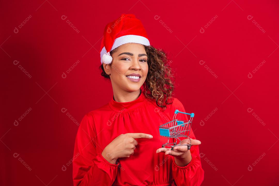 Mulher afro no chapéu de Papai Noel fazendo compras de Natal. Ela está mostrando