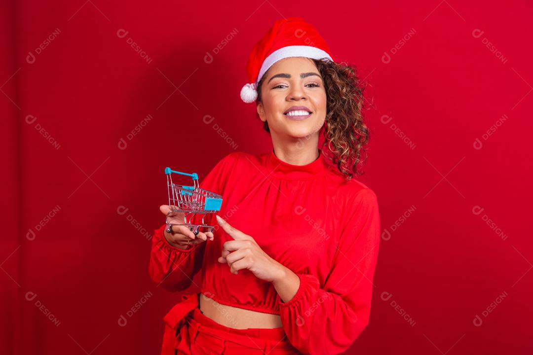 Mulher afro no chapéu de Papai Noel fazendo compras de Natal. Ela está mostrando