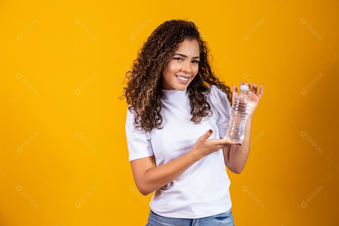 Mulher segurando uma garrafa de água em fundo amarelo. Beber água