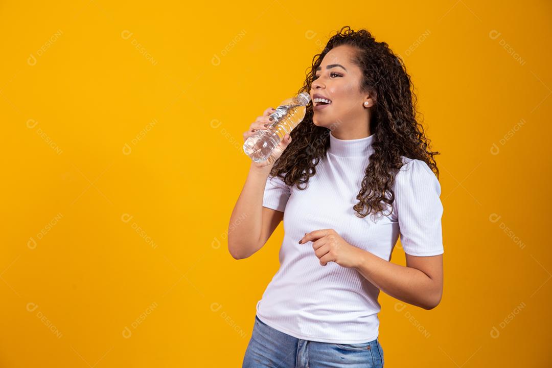 Mulher segurando uma garrafa de água em fundo amarelo. Beber água