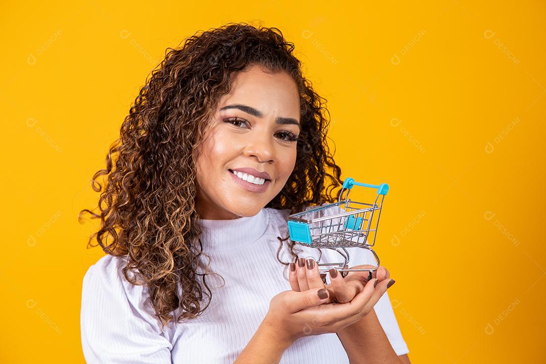 Mulher de cabelo encaracolado sorridente mostrando mini carrinho de compras