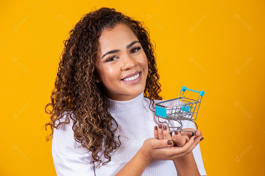Mulher de cabelo encaracolado sorridente mostrando mini carrinho de compras
