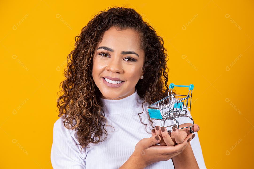Mulher de cabelo encaracolado sorridente mostrando mini carrinho de compras