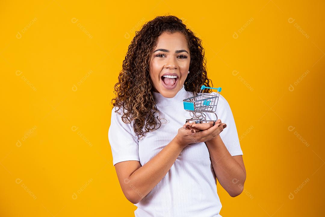 Mulher de cabelo encaracolado sorridente mostrando mini carrinho de compras