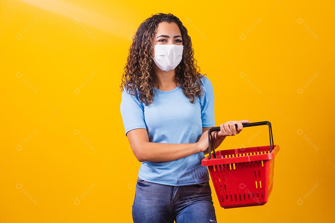 Jovem afro-americana com tranças usando cesta de compras e máscara médica