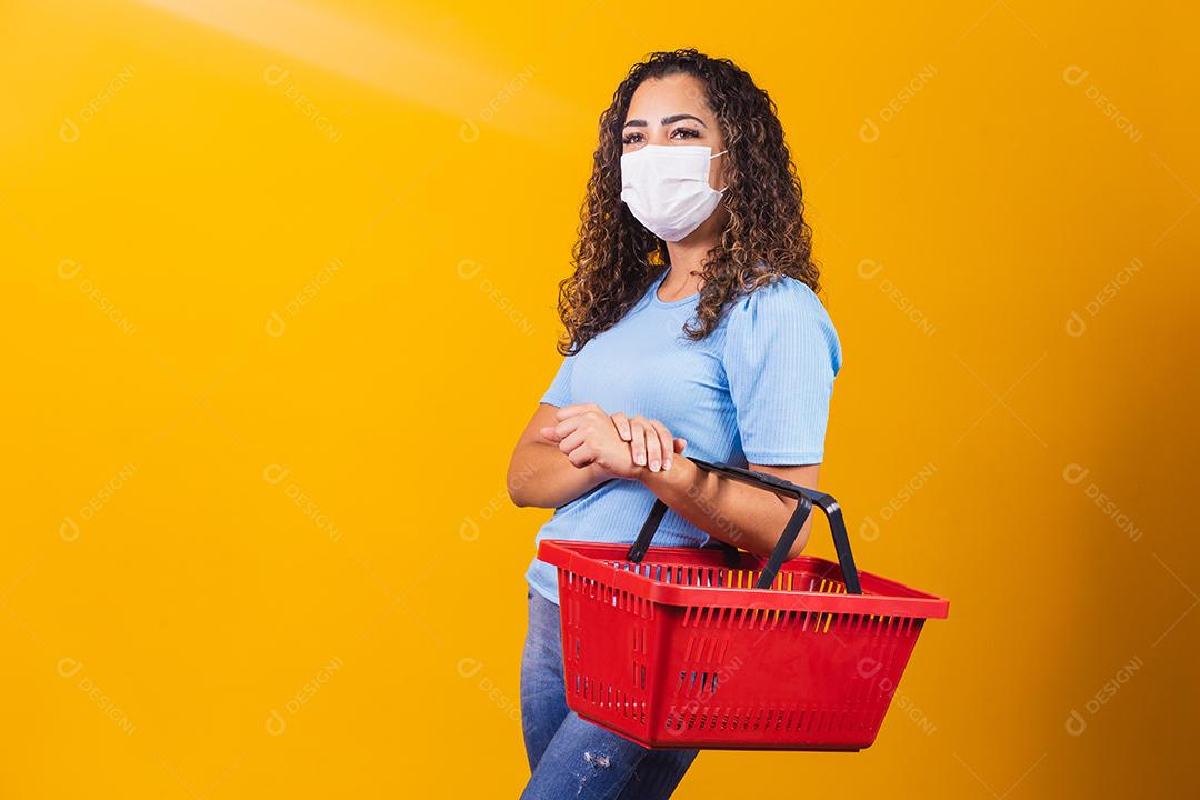 Jovem afro-americana com tranças usando cesta de compras e máscara médica