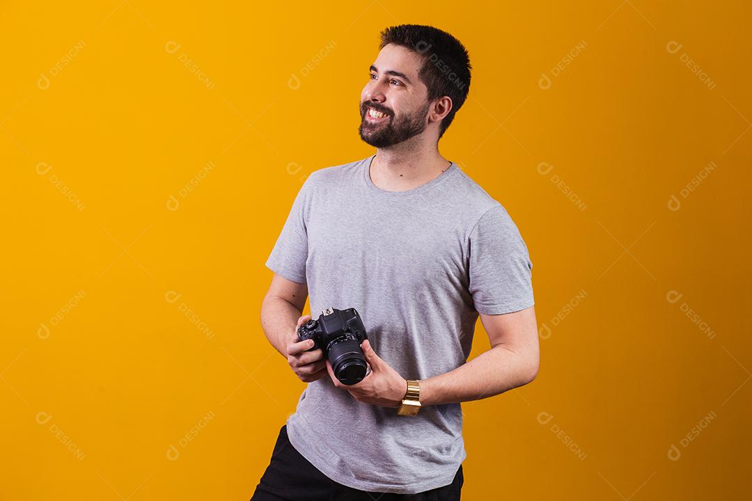 Rapaz com uma câmera fotográfica na mão. Belo fotógrafo em um fundo amarelo