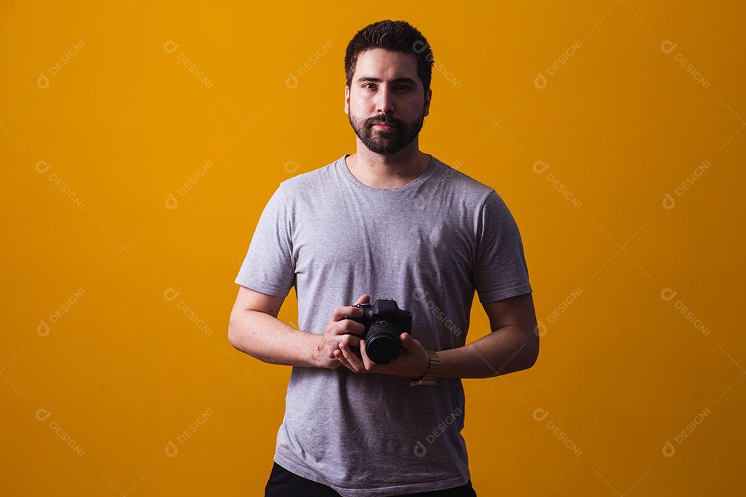 Rapaz com uma câmera fotográfica na mão. Belo fotógrafo em um fundo amarelo