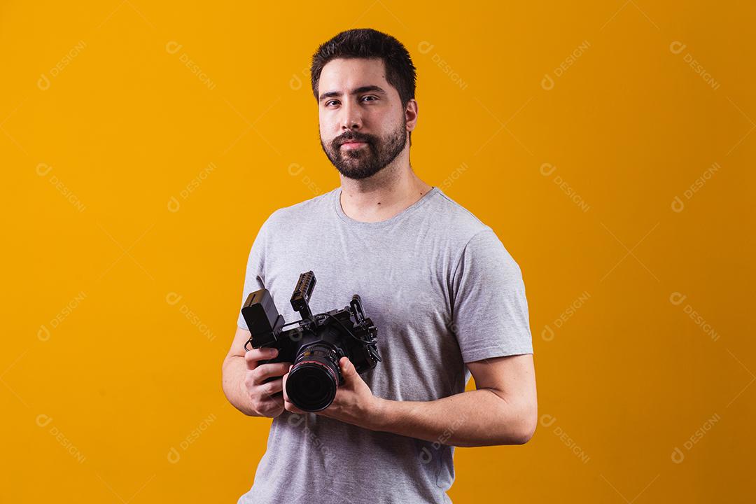 Rapaz com uma câmera fotográfica na mão. Belo fotógrafo em um fundo amarelo