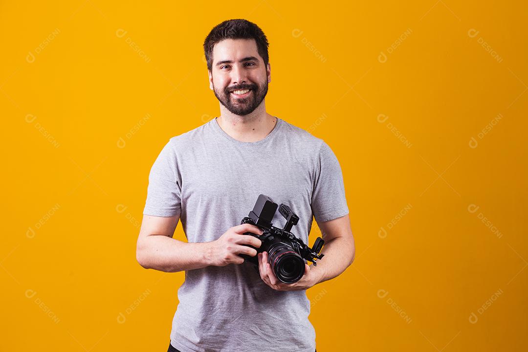 Rapaz com uma câmera fotográfica na mão. Belo fotógrafo em um fundo amarelo