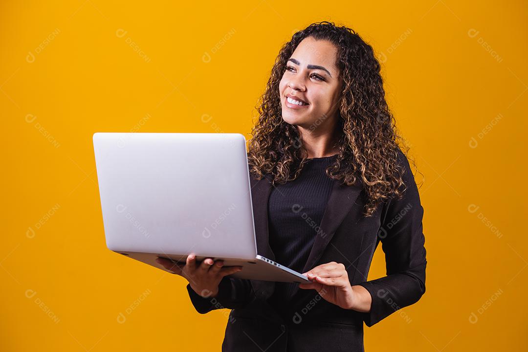 Retrato de jovem com roupa de executivo com laptop em fundo amarelo. Empresária trabalhando com laptop