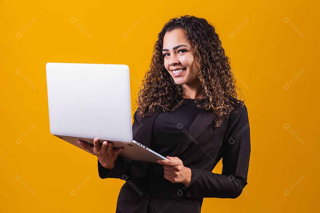 Retrato de jovem com roupa de executivo com laptop em fundo amarelo. Empresária trabalhando com laptop