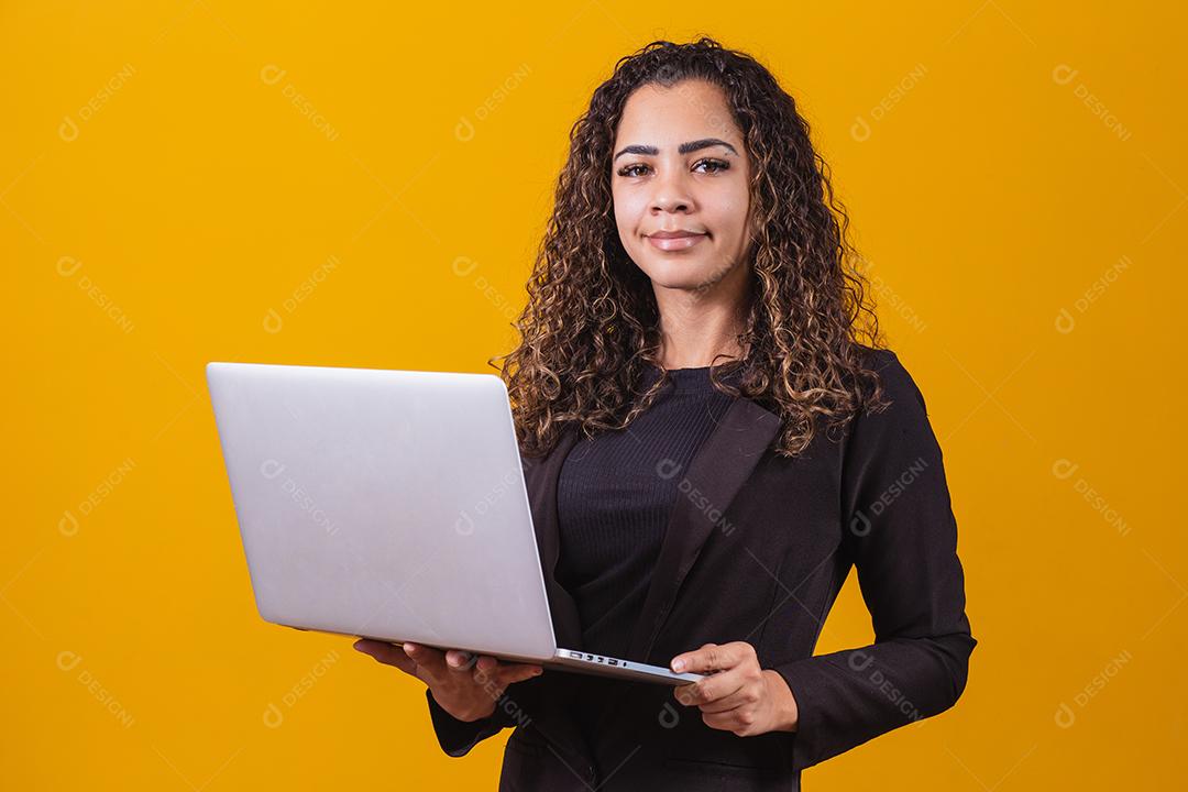 Retrato de jovem com roupa de executivo com laptop em fundo amarelo. Empresária trabalhando com laptop