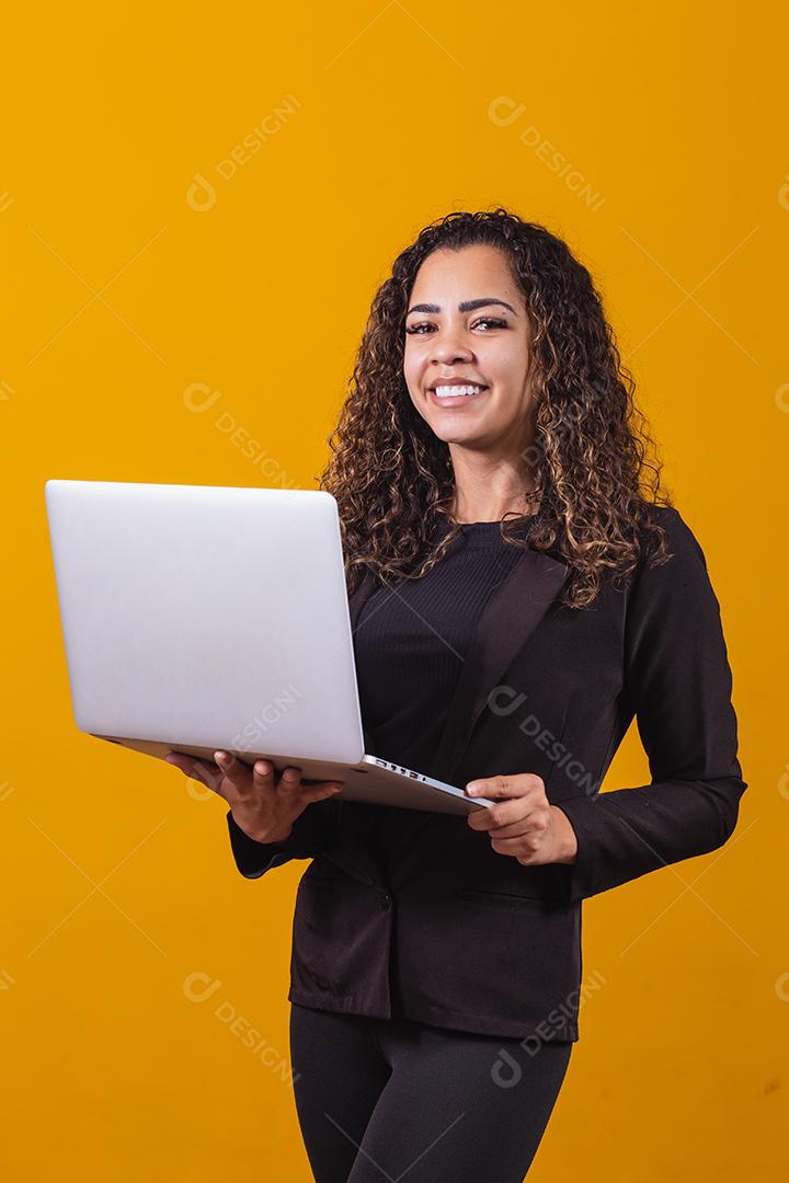 Retrato de jovem com roupa de executivo com laptop em fundo amarelo. Empresária trabalhando com laptop