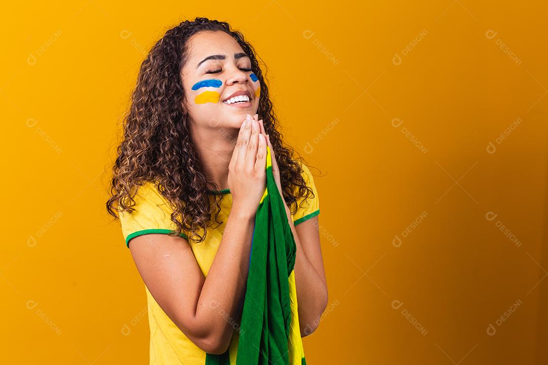 fã brasileiro com bandeira rezando sobre fundo amarelo. orando pelo brasil