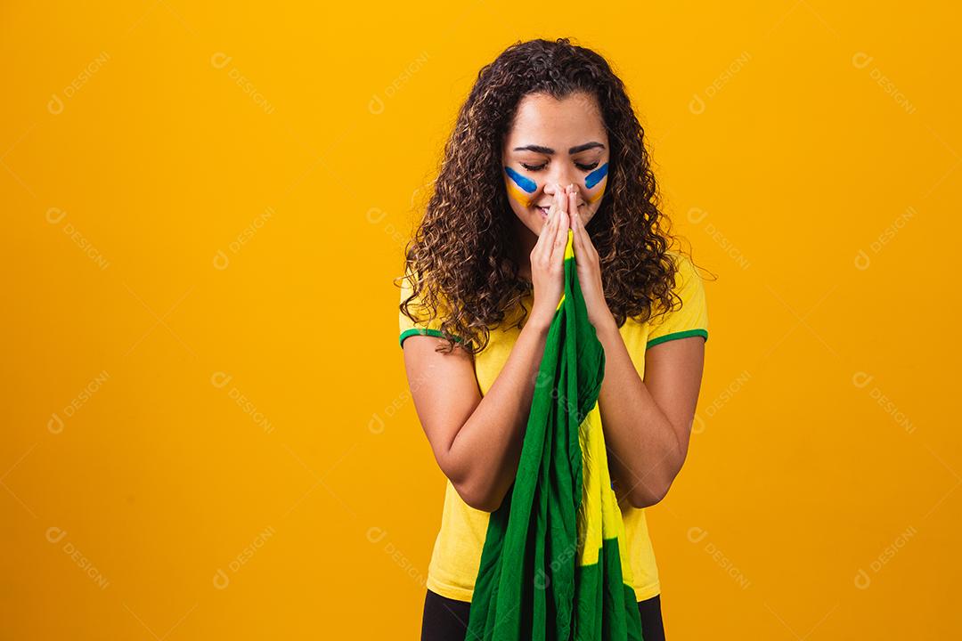 fã brasileiro com bandeira rezando sobre fundo amarelo. orando pelo brasil