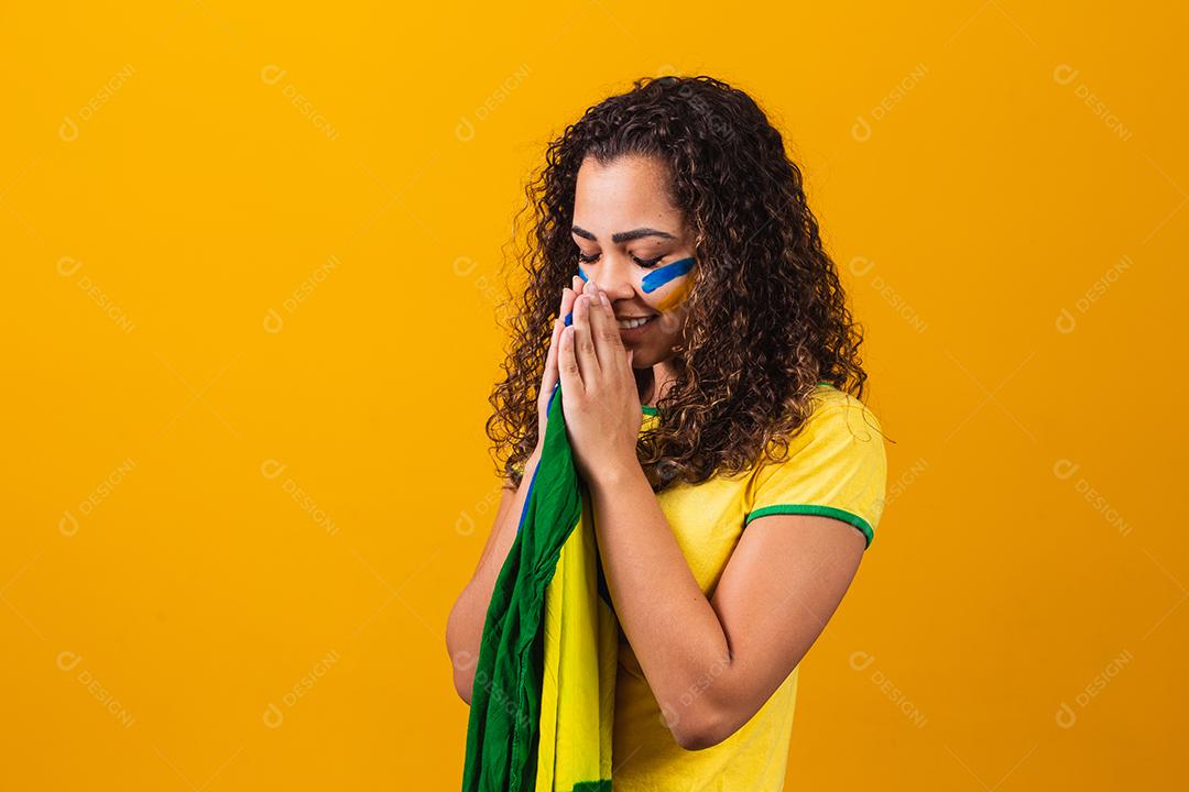 fã brasileiro com bandeira rezando sobre fundo amarelo. orando pelo brasil