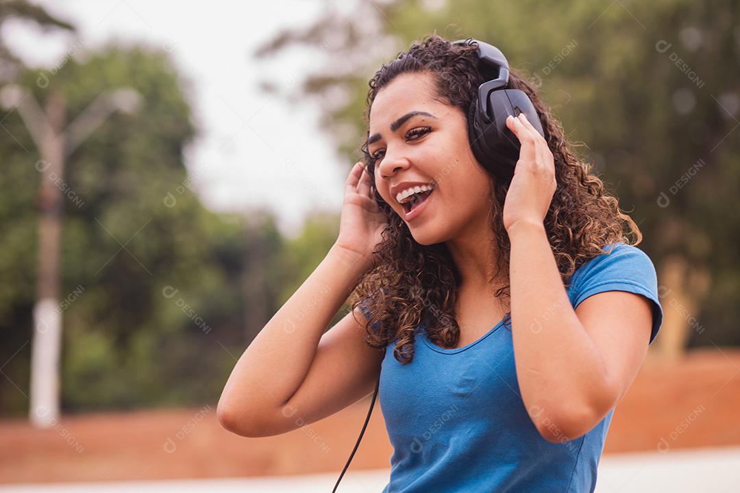 Mulher afro feliz ouvindo música em seu fone de ouvido.