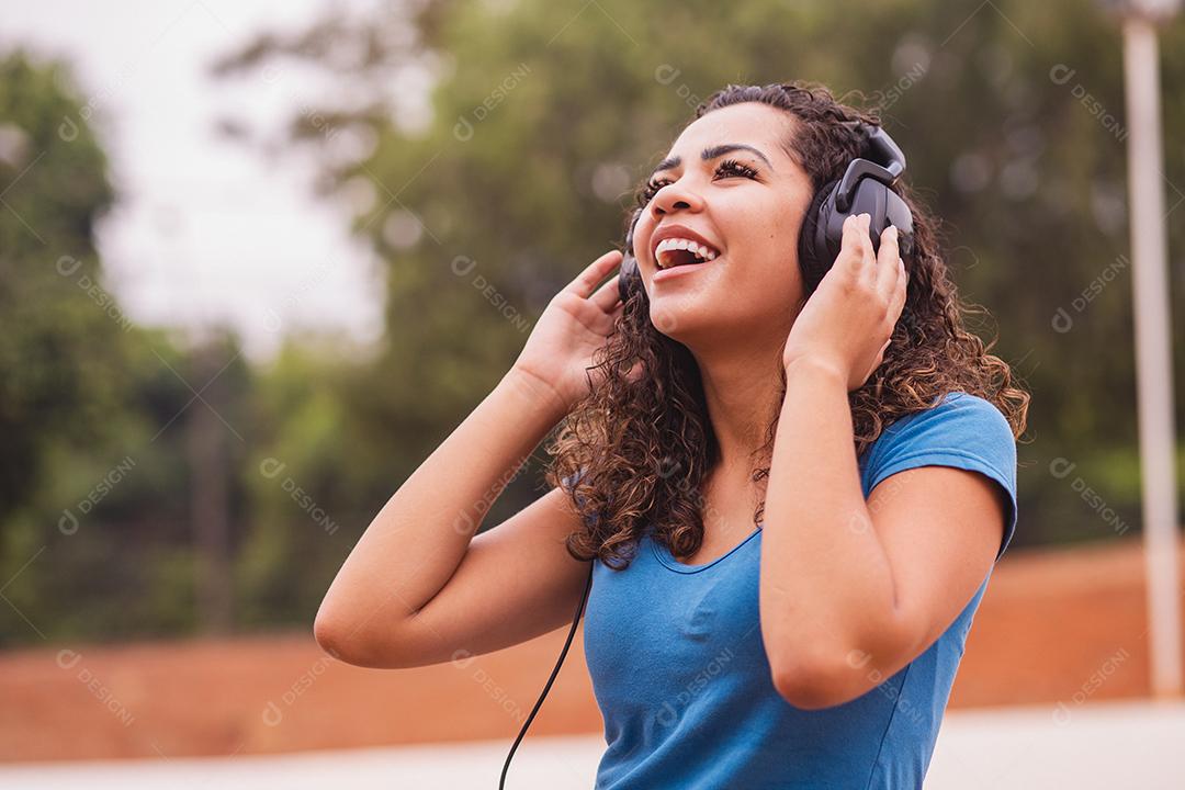 Mulher afro feliz ouvindo música em seu fone de ouvido.