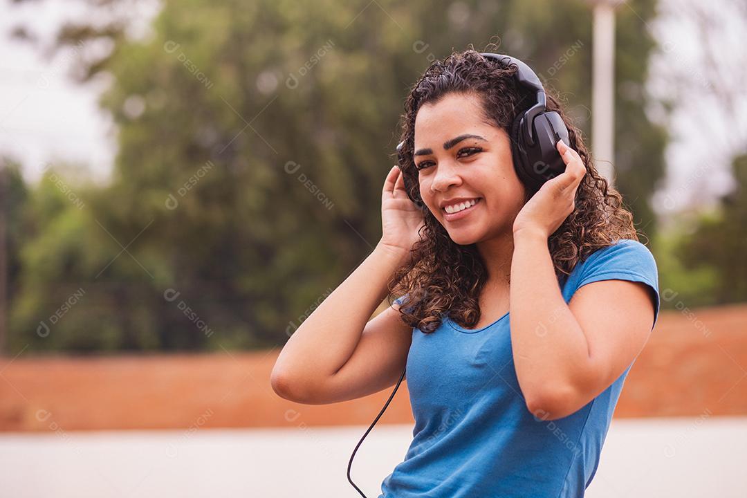 Mulher afro feliz ouvindo música em seu fone de ouvido.