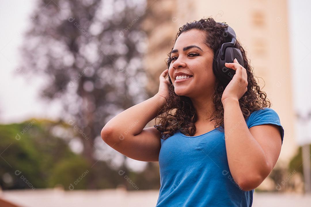 Mulher afro feliz ouvindo música em seu fone de ouvido.