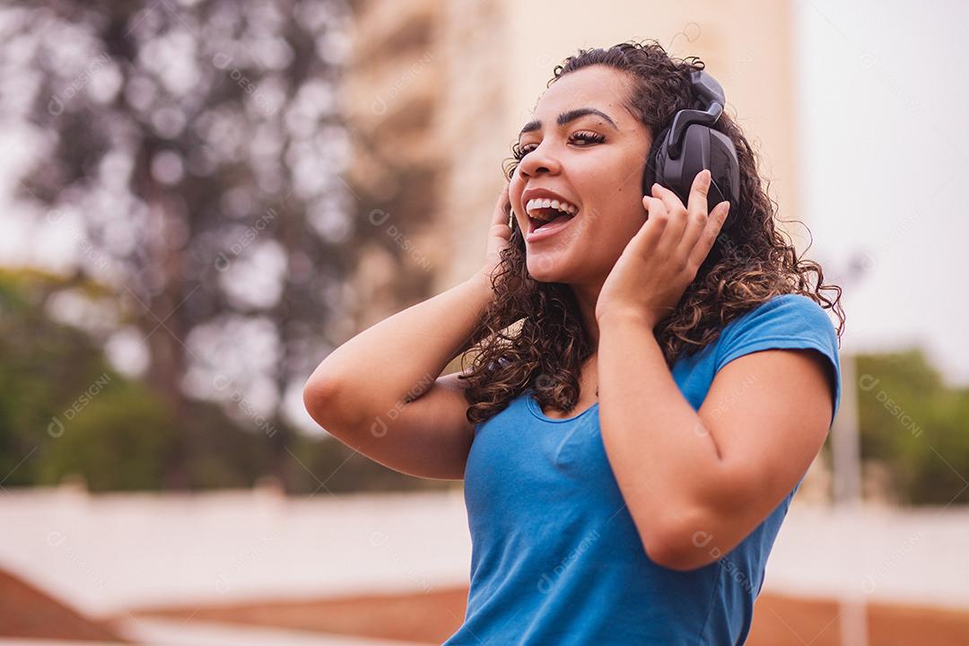 Mulher afro feliz ouvindo música em seu fone de ouvido.