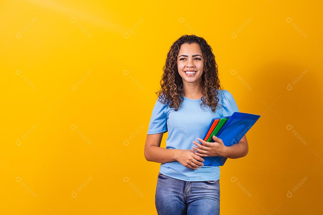 Jovem estudante adolescente afro-americano em roupas casuais, segurando livros isolados no retrato de estúdio