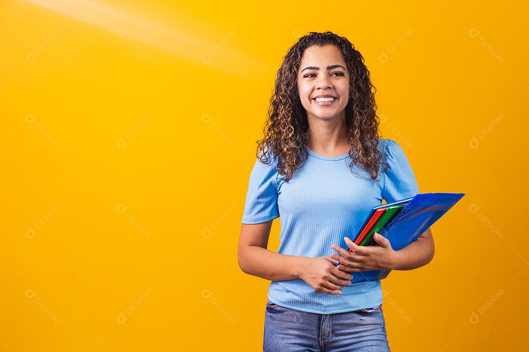 Jovem estudante adolescente afro-americano em roupas casuais, segurando livros isolados no retrato de estúdio