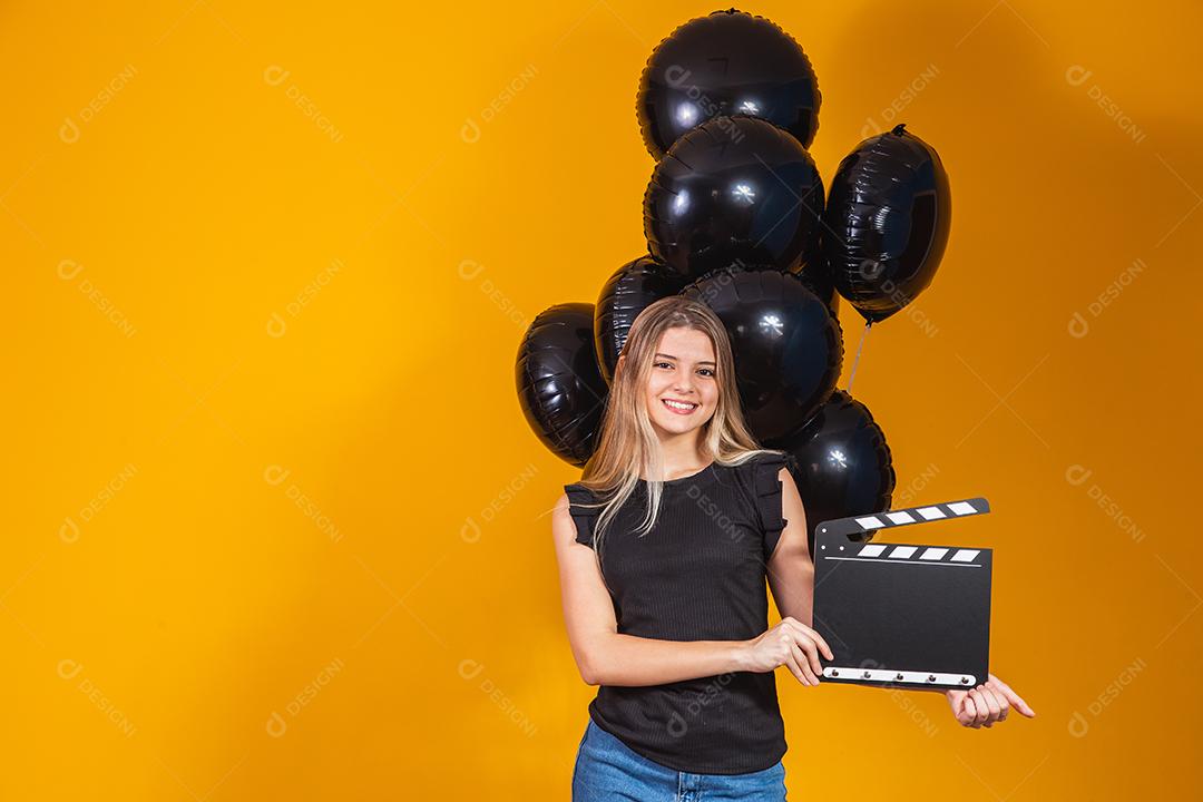Jovem mulher rindo segurando filme preto clássico fazendo claquete e comemorando com balões de ar preto isolados