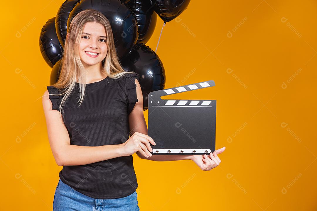 Jovem mulher rindo segurando filme preto clássico fazendo claquete e comemorando com balões de ar preto isolados
