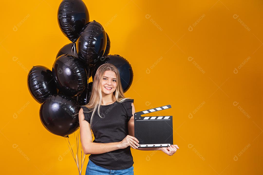 Jovem mulher rindo segurando filme preto clássico fazendo claquete e comemorando com balões de ar preto isolados