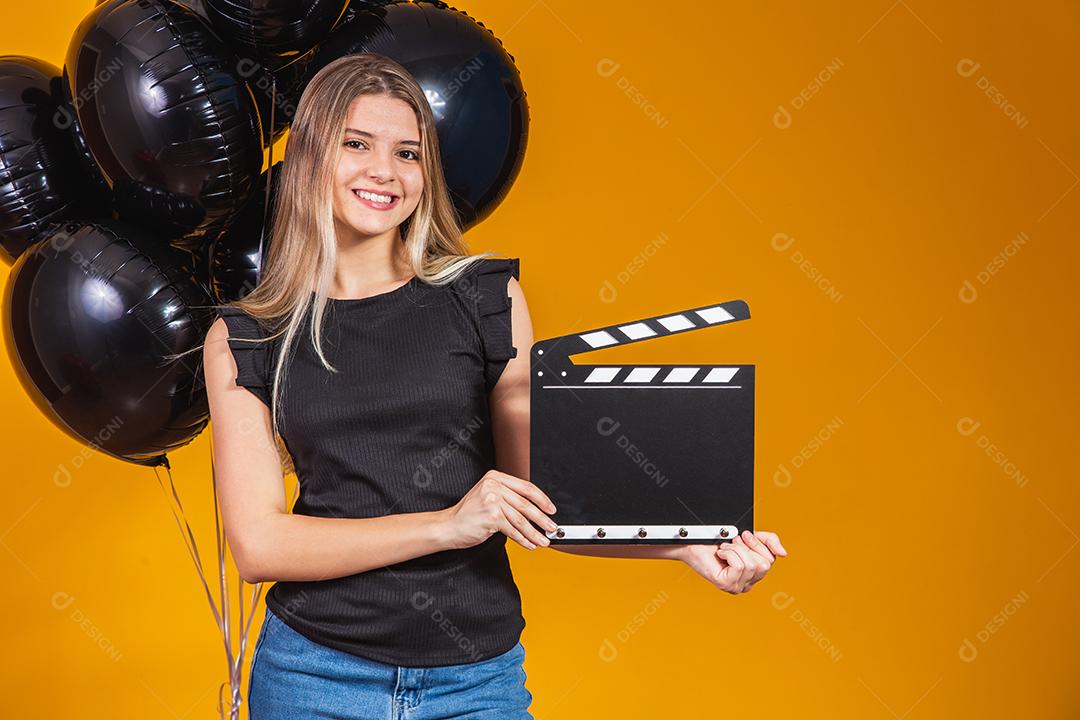 Jovem mulher rindo segurando filme preto clássico fazendo claquete e comemorando com balões de ar preto isolados