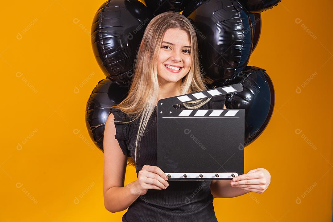 Jovem mulher rindo segurando filme preto clássico fazendo claquete e comemorando com balões de ar preto isolados