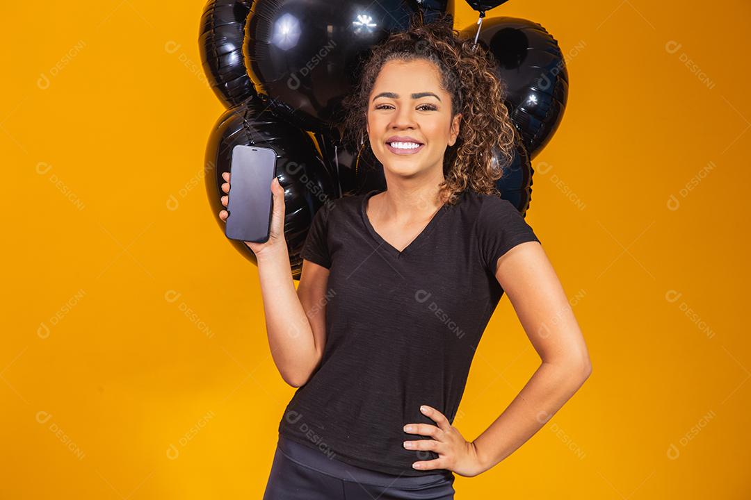 Sorrindo encantadora jovem afro segurando um celular com tela em branco vazia sobre fundo amarelo