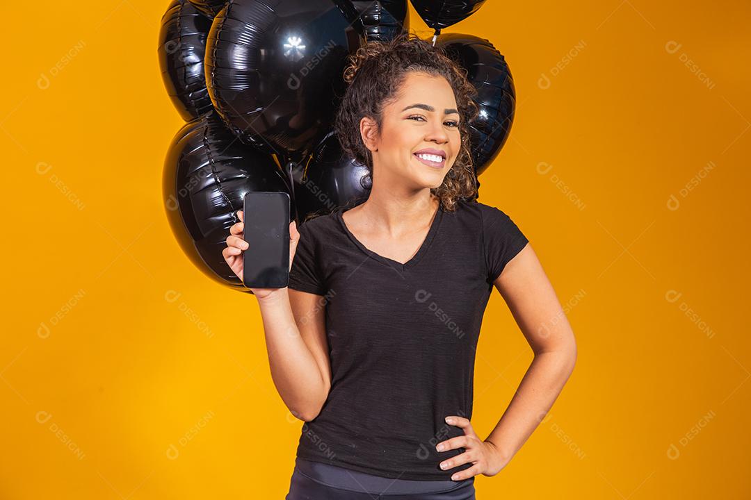 Sorrindo encantadora jovem afro segurando um celular com tela em branco vazia sobre fundo amarelo