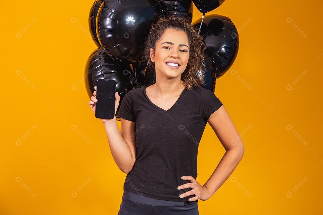 Sorrindo encantadora jovem afro segurando um celular com tela em branco vazia sobre fundo amarelo