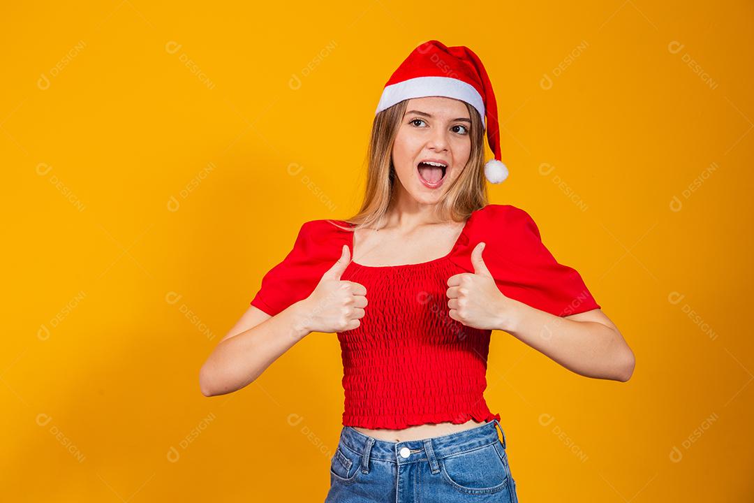 Retrato de mulher alegre mostrando os polegares usando chapéu de Papai Noel.