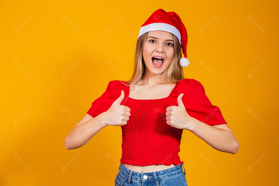 Mulher loira bonita positiva com chapéu de Papai Noel e roupa vermelha para o natal. Jovem mulher vestida para o Natal sorrindo.